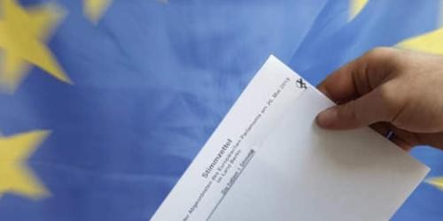 Symbolbild Hand mit gefaltetem Stimmzettel vor dem Hintergrund einer Europafahne