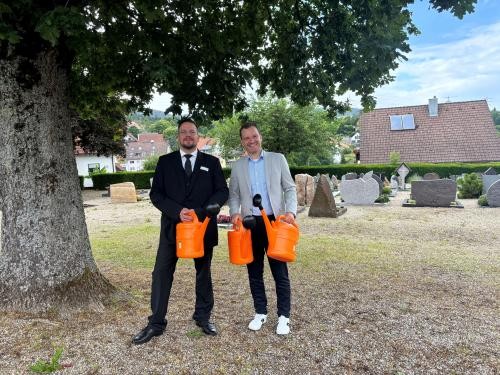 Stefan Merli (links) und Bürgermeister Robert Stiebler mit einigen orangen Gießkannen auf dem Forbacher Friedhof